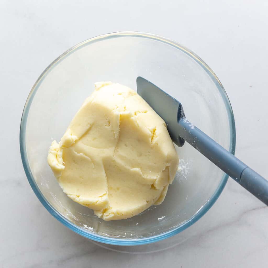 A soft, thick dough made of mashed potato, flour, salt and baking powder in a mixing bowl.