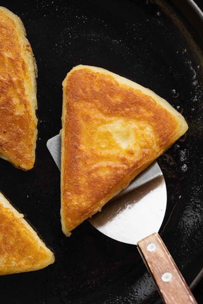 A slice of gluten free Irish Potato Bread scooped up on a spatula from a cast iron skillet.