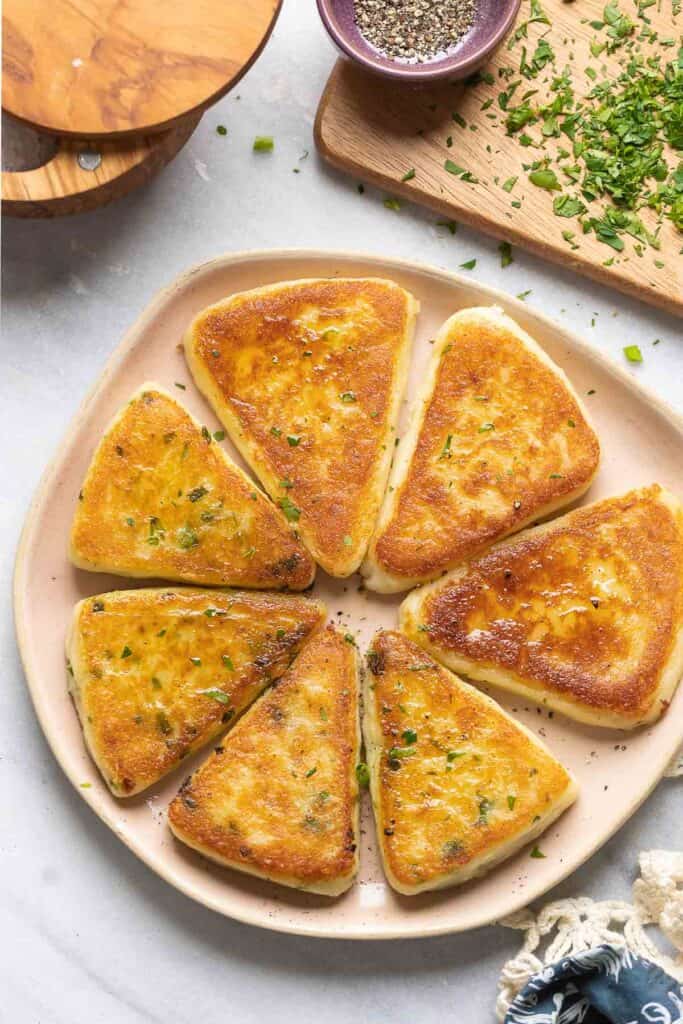 A plate with 7 slices of gluten free Irish potato farls on a plate - 4 chives pieces and 3 cheesy pieces.