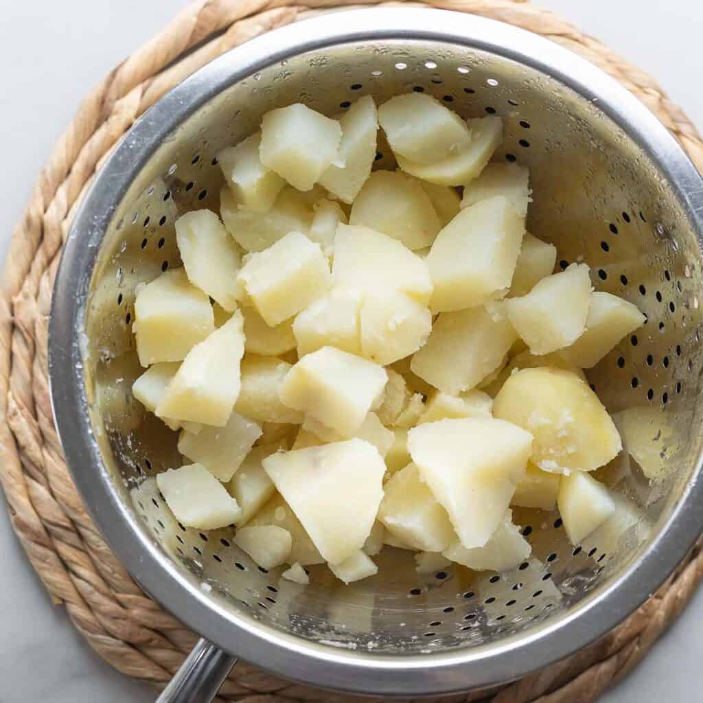 A colander full of roughly chopped, boiled potatoes sitting over a pot. 