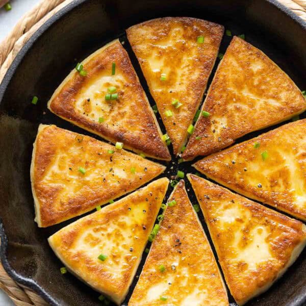 Eight slices of Irish potato bread in a skillet with fresh chives and black pepper sprinkled over top.