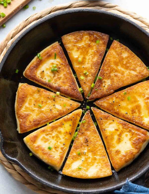 Eight slices of Irish potato bread in a skillet with fresh chives and black pepper sprinkled over top.