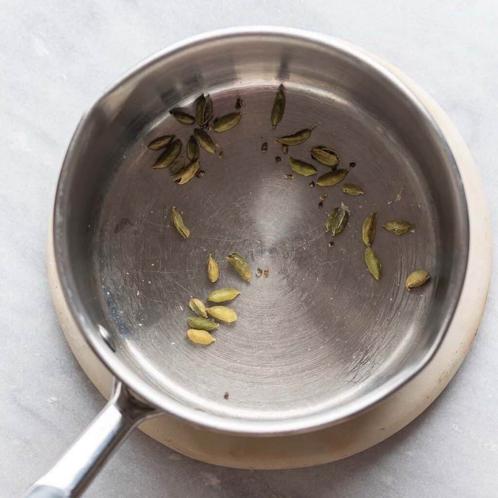 Cardamom pods toasting in a pan.