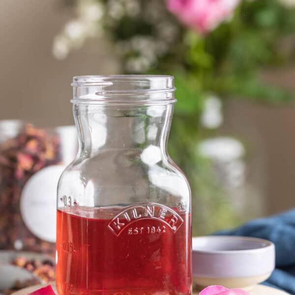 Cardamom Rose Simple Syrup in a kilner storage jar surrounded by rose petals and cardamom pods