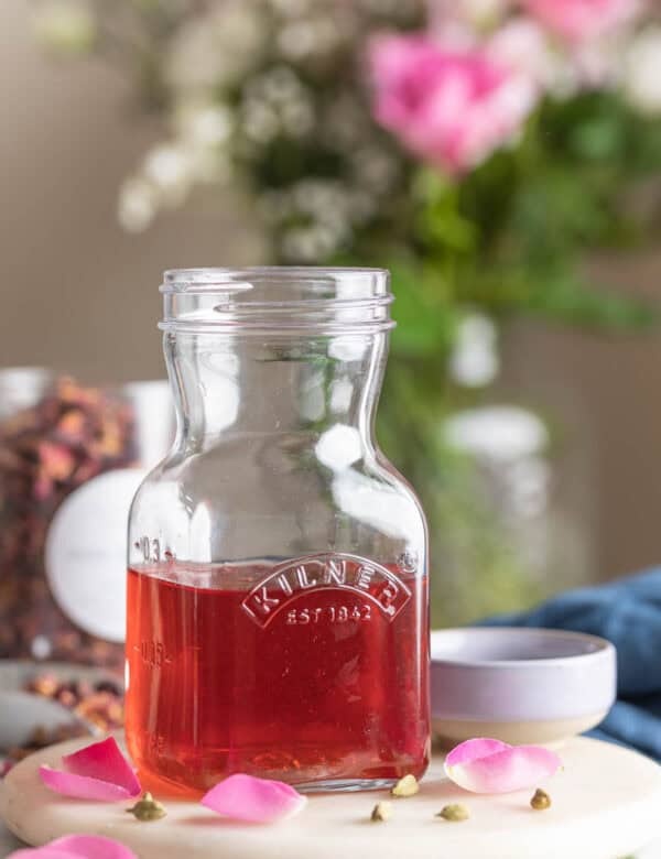 Cardamom Rose Simple Syrup in a kilner storage jar surrounded by rose petals and cardamom pods