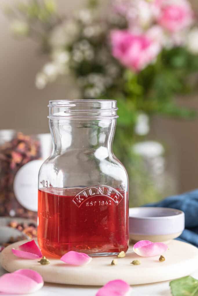 Cardamom Rose Simple Syrup in a kilner storage jar surrounded by rose petals and cardamom pods