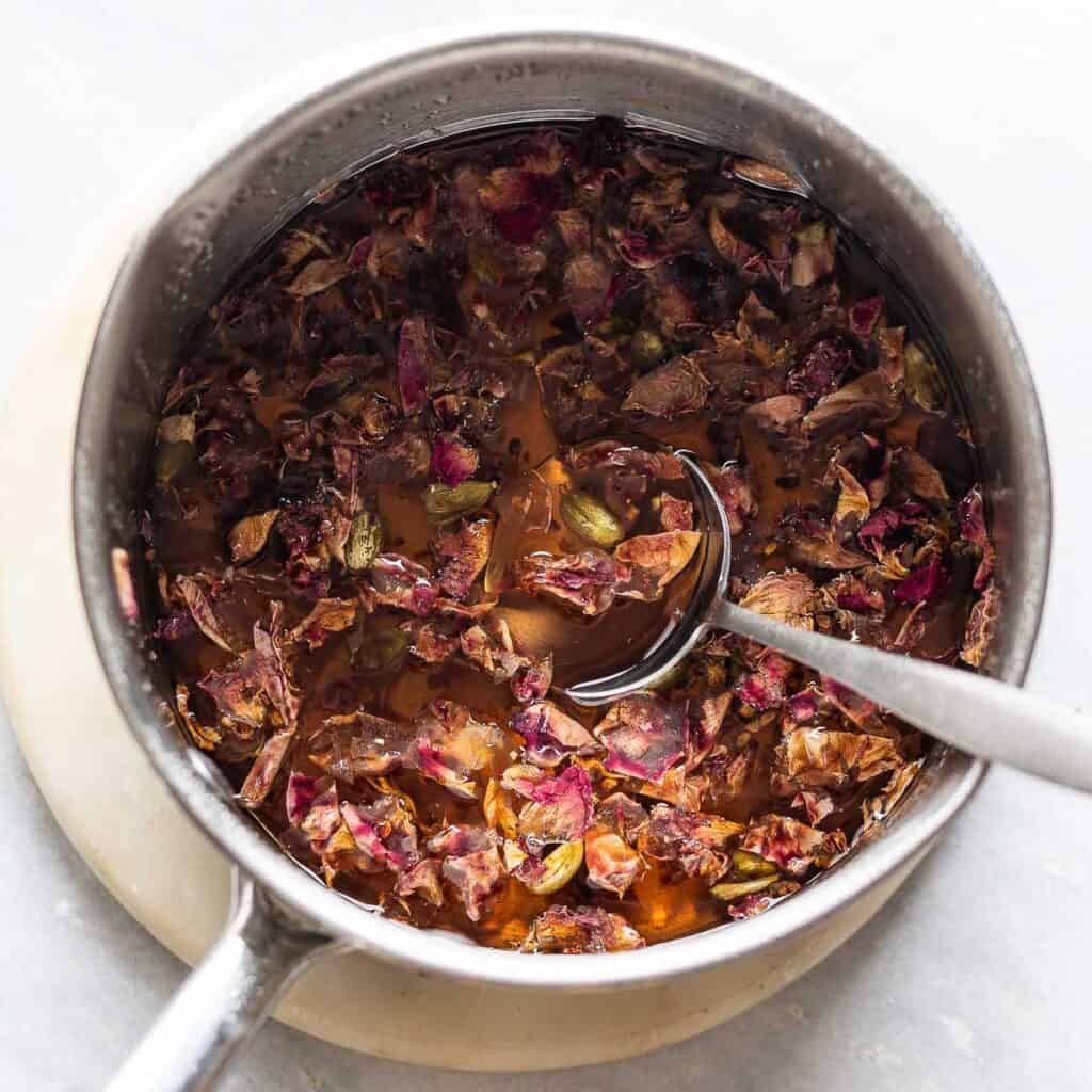 A saucepan full of ingredients for a homemade rose syrup before heating: rose petals, cardamom and sugar.