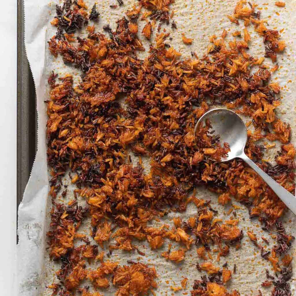 Baked rice, seasoned with a red curry paste mixture spread across a baking sheet with a spoon mixing the rice.