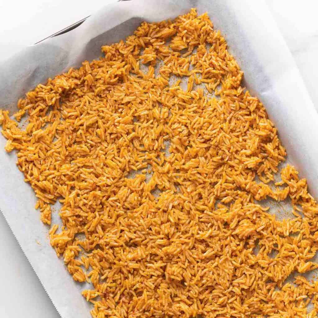 Rice, seasoned with a red curry paste mixture spread across a baking sheet before baking.