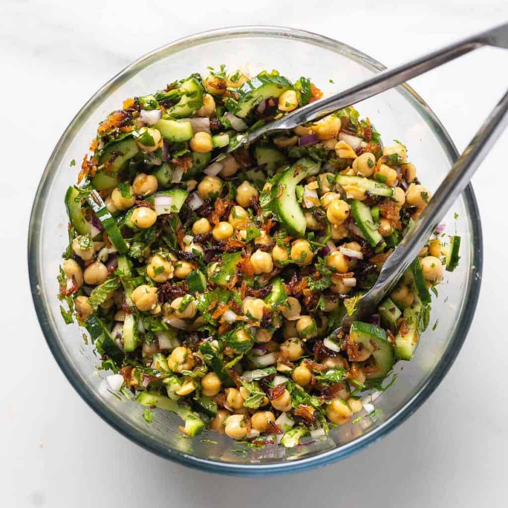 Crispy Rice Salad with Lemony Chickpeas & Cucumber in a bowl with tongs to mix everything together.