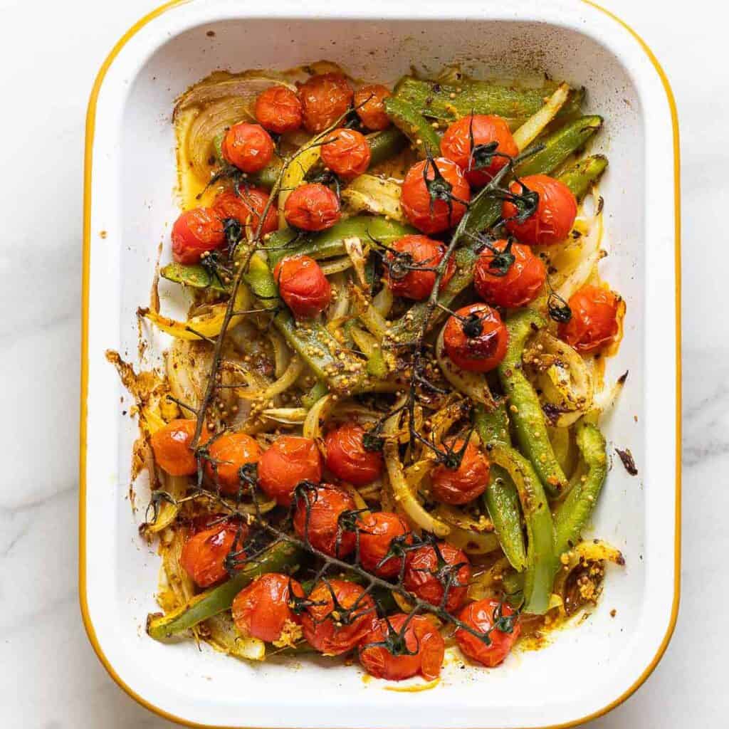 Roasted sliced onions, bell pepper and cherry tomatoes on the vine in a roasting pan tossed in oil and spices.