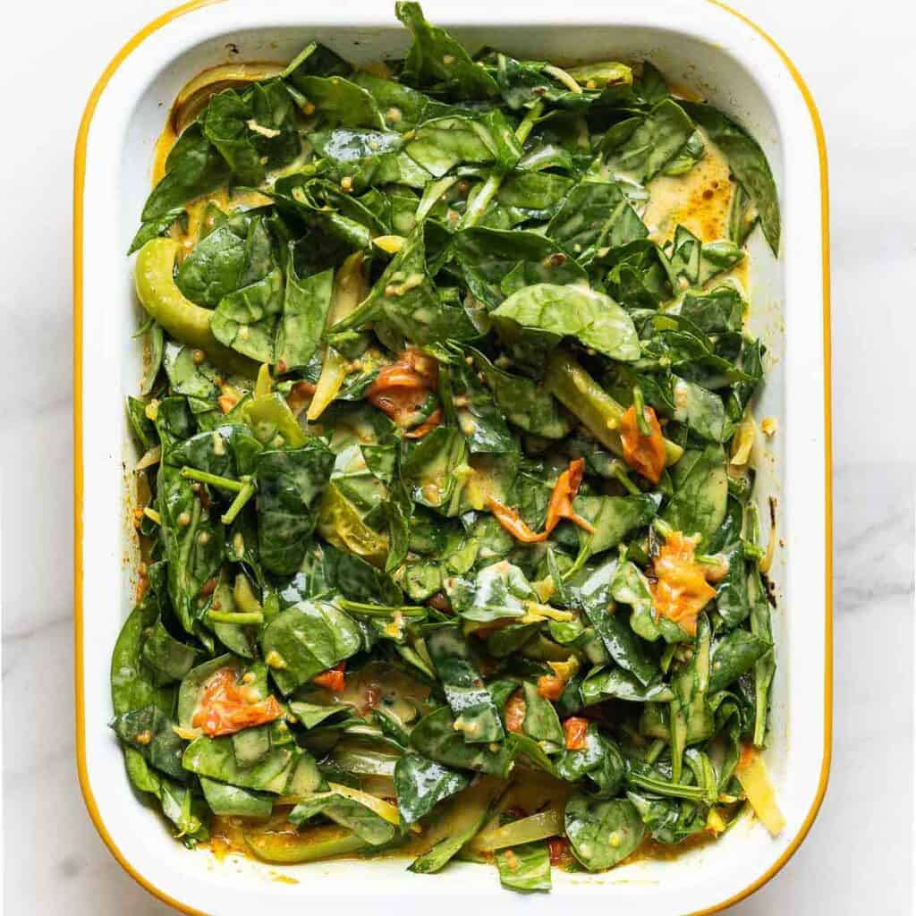 A roasting pan full of roasted vegetables mixed together with raw spinach and coconut milk.