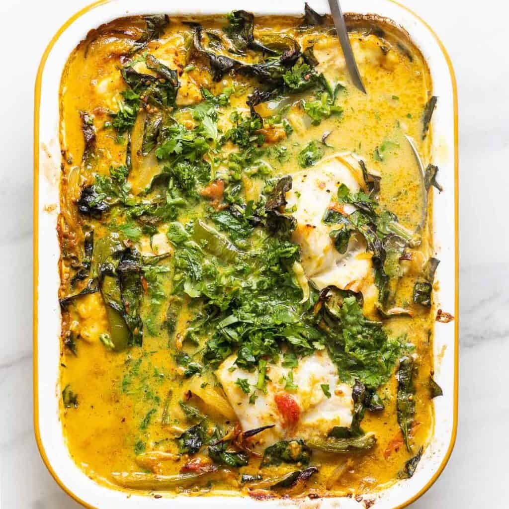 A roasting pan full of a coconut baked fish curry with lime juice and cilantro scattered on top.