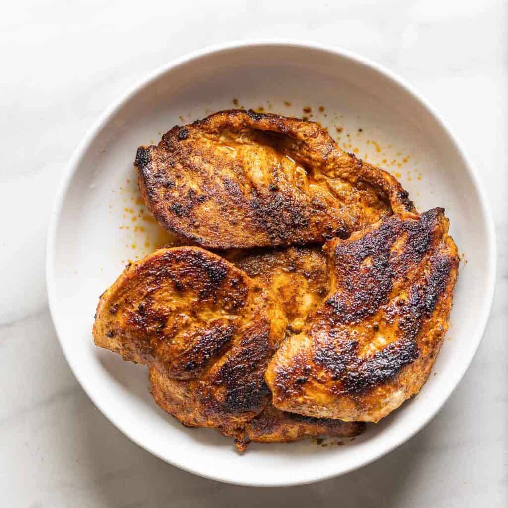 Pan cooked, fajita seasoning chicken breasts resting in a bowl.