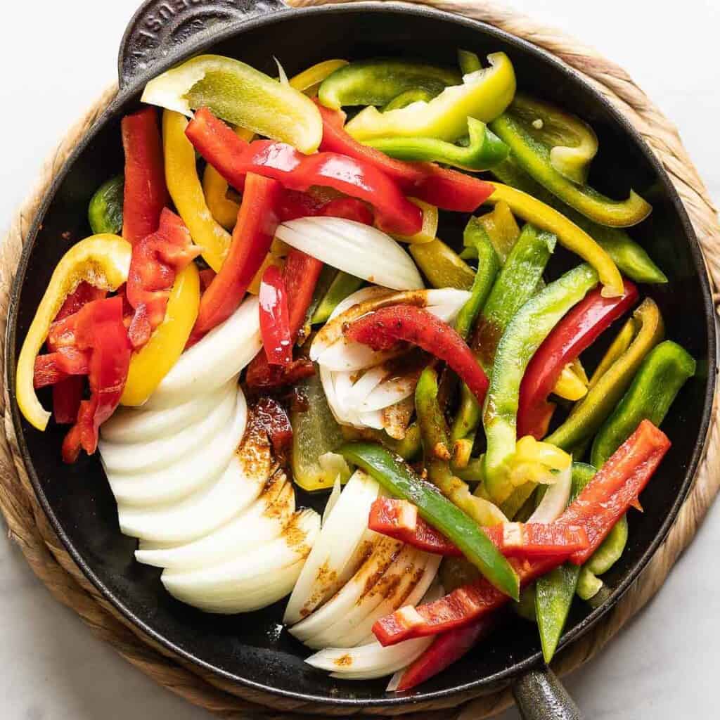 Sliced bell peppers and onion in a cast iron skillet with the leftover fajita marinade drizzled over the top.