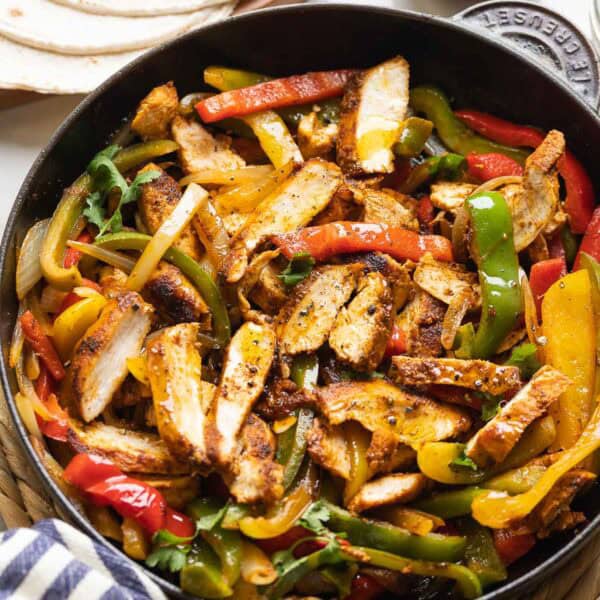 Homemade Chicken Fajitas in a cast iron skillet: sliced chicken breast, sautéd bell peppers and onions mixed together with flour tortillas and guacamole on the side.