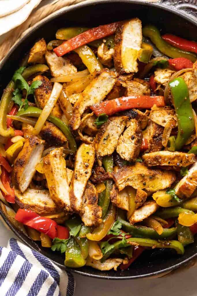 A cast iron skillet full of homemade chicken fajitas: sliced chicken breast mixed with sautéd peppers and onions.