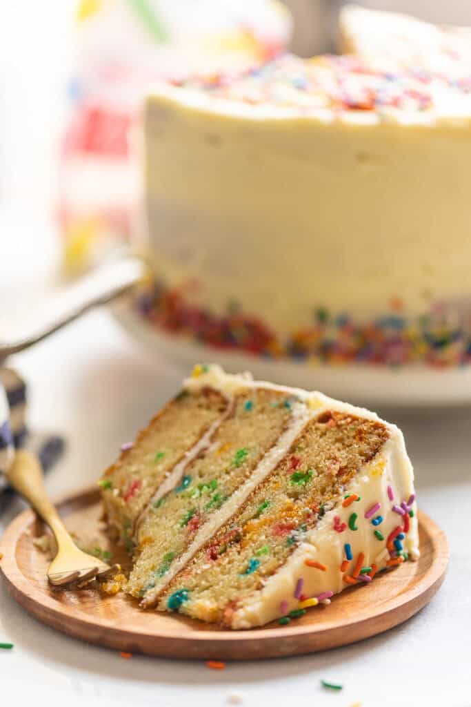 A slice of a vanilla frosted gluten free funfetti cake on a plate with a bite taken out.