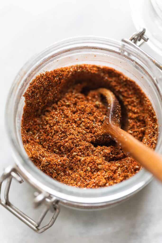 Homemade Fajita Spice Mix in a small storage jar with a wooden spoon.