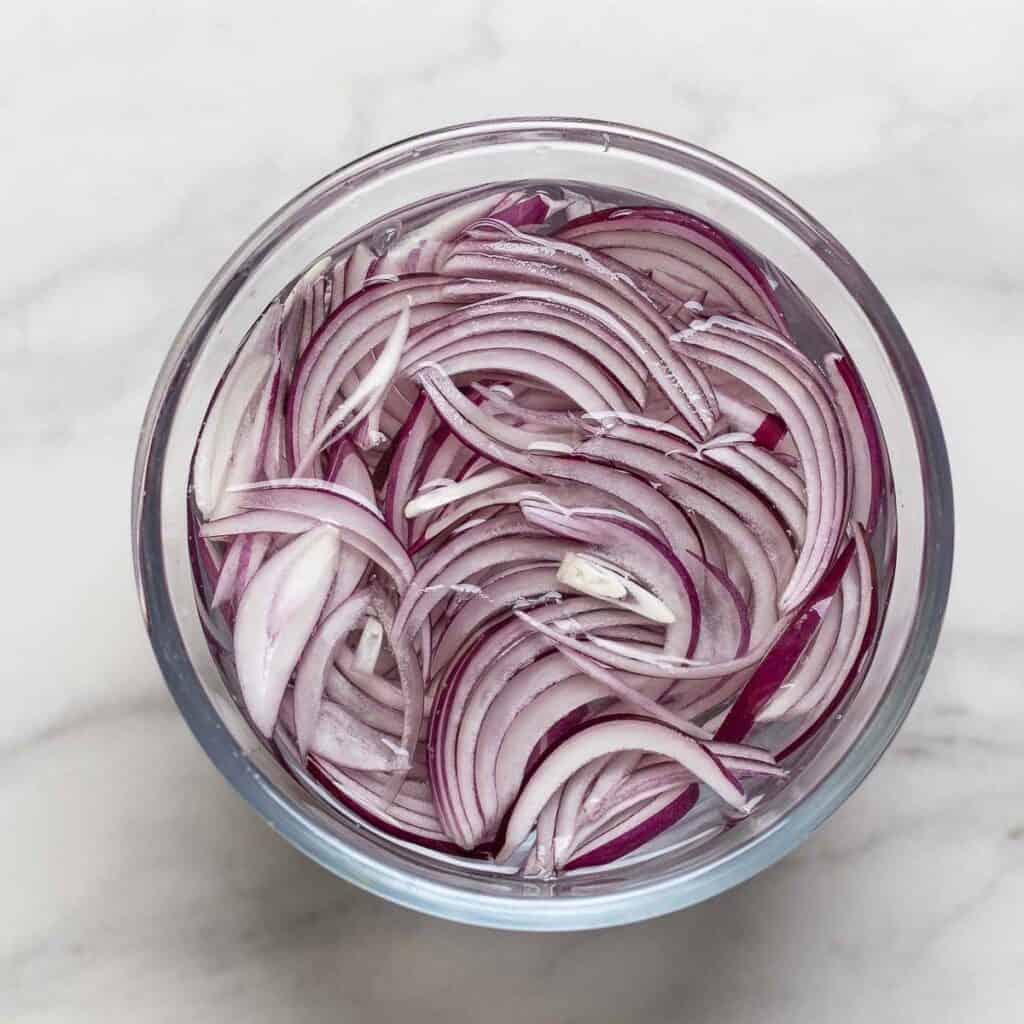 Thinly sliced red onion covered in a bowl with cold water.