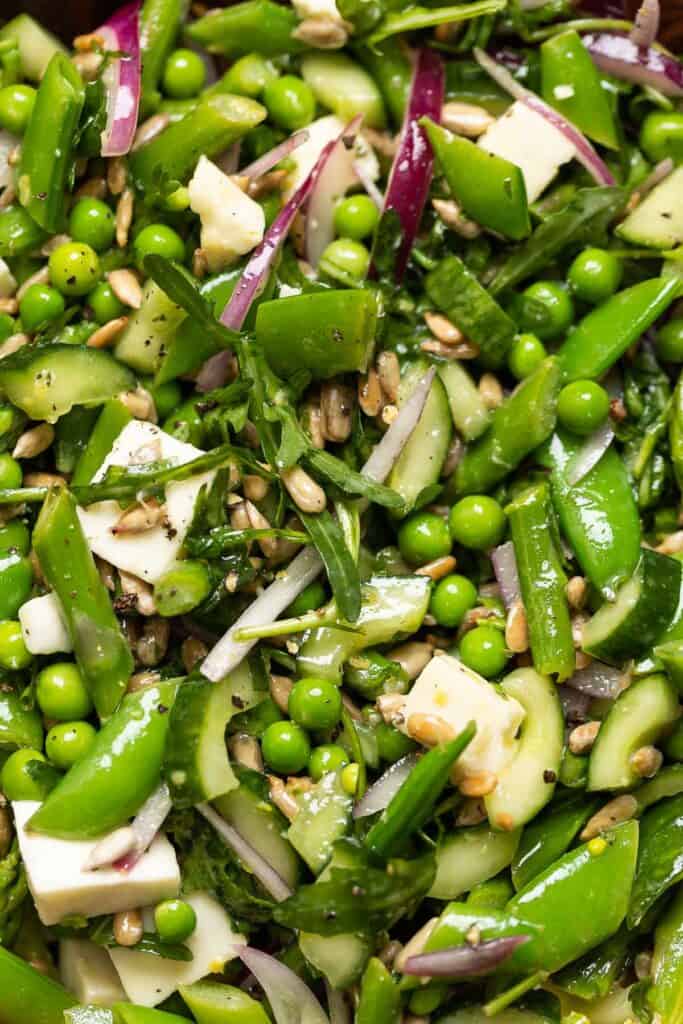 A salad made up of snap peas, english peas, asparagus, arugula, cucumber, onion, mozzarella and sunflower seeds.